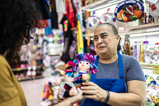 Mid adult woman taking mexican doll from senior woman at a gift shop