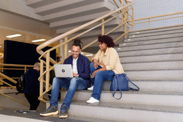 istock Classmates using a laptop while sitting on the stairs inside the university campus 1415644661