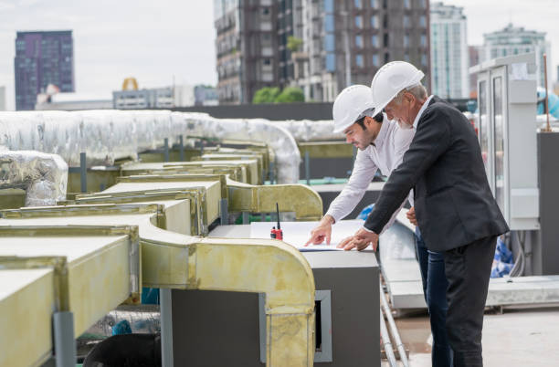istock Two engineer discuss about project on building plan or drawing and stay near air vents of construction site. 1415649428