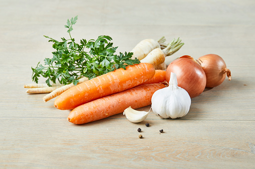 Fresh seasoning on a rustic kitchen table, including carrot, parsley, garlic and onion, for soup preparation