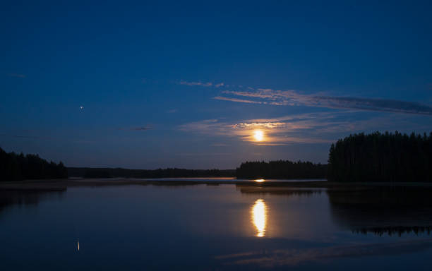 Moonlight night by the lake. Full moon and planet Jupiter in the sky and reflecting on water surface. stock photo