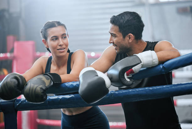 Fit, active and healthy boxing team bonding after workout, training and exercise in a wellness center. Sporty, athletic or strong man and woman on break from kickboxing fight and sports match in ring