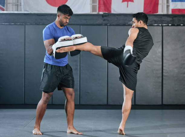 Active, athletes and fit men doing sport training workout and kick boxing on a gym mat. Diverse male pair or MMA boxer and trainer practice sparring exercises for a healthy wellness lifestyle. activos, atletas y hombres en forma kick boxing y haciendo entrenamiento deportivo en un gimnasio. dos compañeros masculinos o boxeadores y entrenadores de mma practican ejercicios de sparring para un estilo de vida saludable y de bienestar.