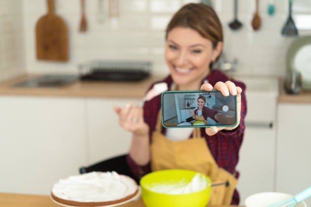 istock Young woman making a cake and vlogging about it 1415653299