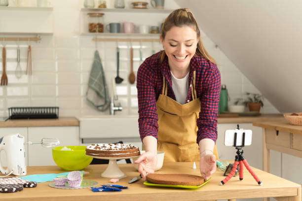 istock Happy young woman making a cake and filming a vlog about it 1415653323