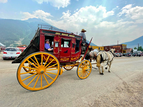 Silverton, Colorado, USA - July 12, 2021: A tourist waves out the open window of a horse-drawn stagecoach during a ride through Silverton’s historic downtown district.