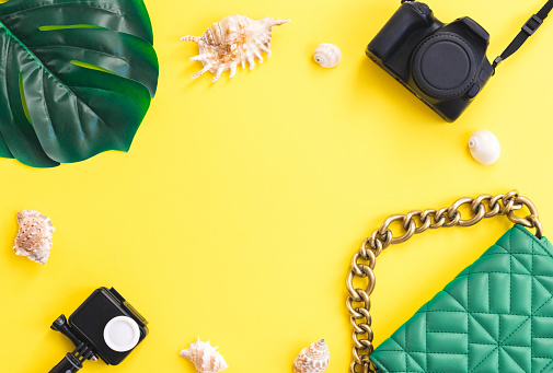 Two cameras, a green bag, a monstera leaf and seashells lie in a round frame on a yellow background with copy space in the center, flat lay close-up. Summer concept, summer blogger, summer time.