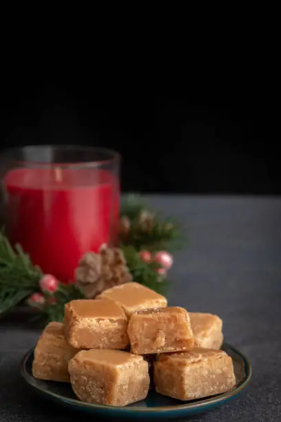 Butterscotch Fudge on Plate with Christmas Candle on Dark Background with Copy Space Vertical