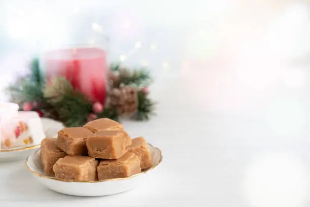 Caramel Fudge on Plate with Christmas Candle and Lights on Light Background with Copy Space Horizontal