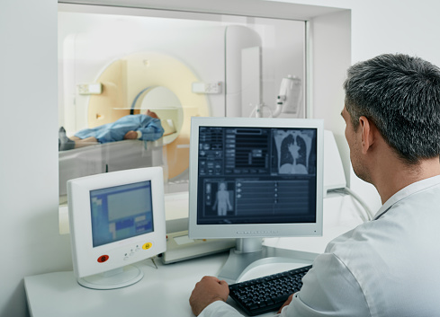 Doctor radiologist running CT scan for patient's body lungs from control room. Computed Tomography