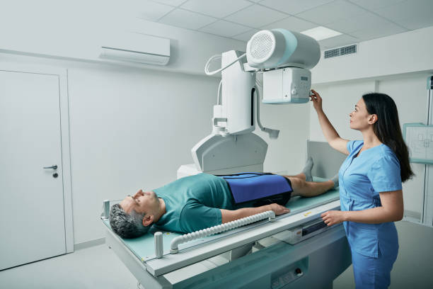 남성 환자는 침대에 누워 여성 간호사가 부상과 골절에 대한 그의 다리 또는 무릎을 스캔하기 위해 현대 x 선 기계를 조정하는 동안 - x ray 뉴스 사진 이미지