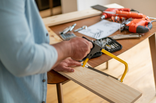 Close-up on a man at home cutting a piece of wood with a hand saw - DIY concepts