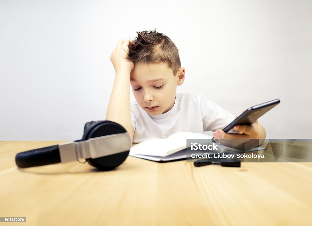 Tired boy with closed eyes sitting at the table on a gray background Tired boy with closed eyes sitting at the table on gray background Boredom Stock Photo