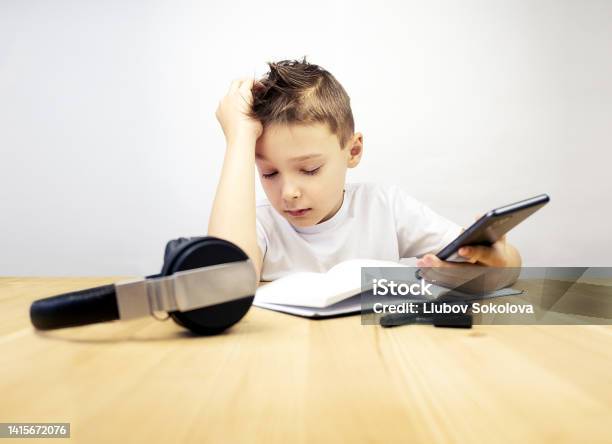 Tired Boy With Closed Eyes Sitting At The Table On A Gray Background Stock Photo - Download Image Now