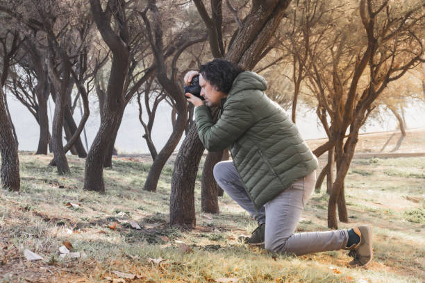 istock Caucasian man taking photo kneeling on forest grass with trees in background 1415677380
