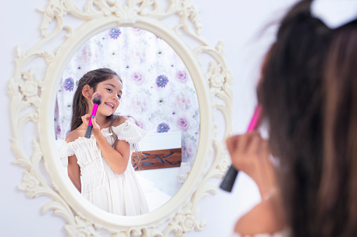 cute little girl doing makeup in front of the mirror