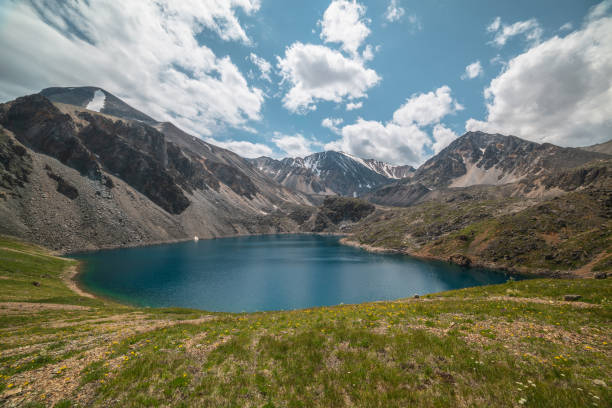 istock Deep mountain lake of phantom blue color among sharp rocks and high mountains in changeable weather. Wonderful dramatic view from sunlit grassy hill to deep blue alpine lake and rocks under cloudy sky 1415682184
