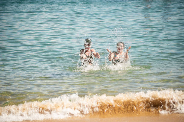 Two women splashing water on the beach at Porto da Barra in Salvador, Bahia.
