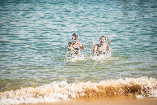 Two women splashing water on the beach at Porto da Barra in Salvador, Bahia.
