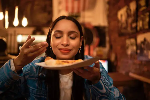 Photo of Hungry woman with delicious pizza, food or consumables at a bar, restaurant or diner at night. One happy and casual girl, foodie or tourist enjoying a dinner meal at a local trendy location