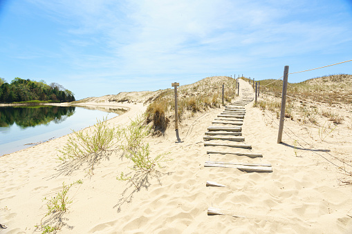 A set of s-curve stairs ascend and sand dune locate in Michigan Sleeping Bear National Lakeshore.  The stairway leads to the blue sky with light white clouds and is adjacent to a small calm lake.