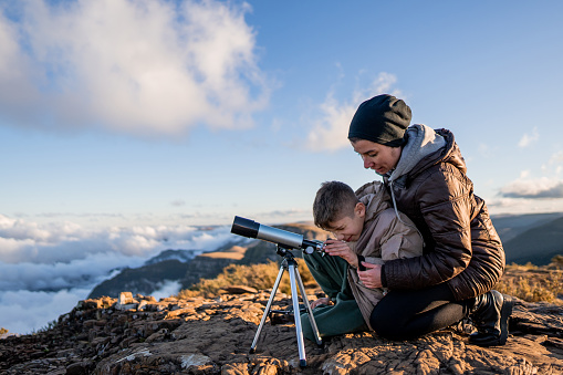 Mother and son looking through the telescope on top of the mountain