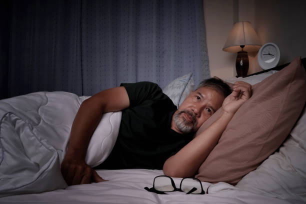 anciano deprimido y estresado acostado en la cama por insomnio - levantarse fotografías e imágenes de stock