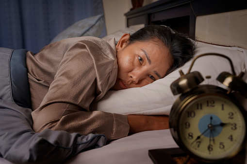 mujer de mediana edad deprimida y estresada acostada en la cama mirando el reloj del insomnio photo