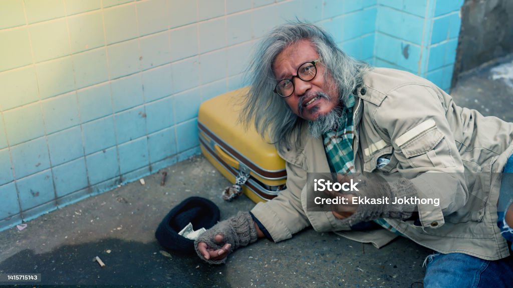 A homeless man, notoriously busy, seeks help from passersby, starving with no food to eat from homelessness and joblessness. The poor man had no home to live streets. 60-64 Years Stock Photo