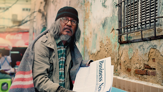Asian homeless people standing like a newspaper in the corner of an old building looking for a job, an old man waiting for hope and help because there is no home and no job stay hungry
