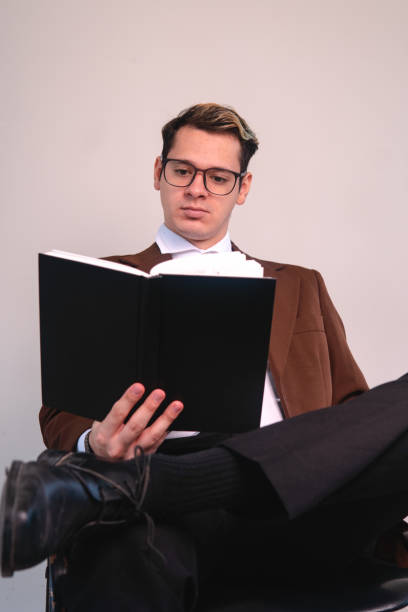 istock An elegantly dressed intellectual man concentrating on the book he is reading. A businessman on a white background. Man in a suit studying with his black notebook. 1415717341