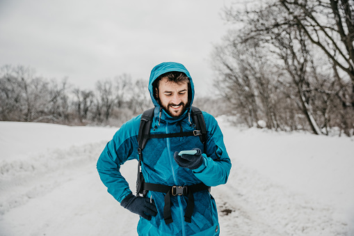 A young man in warm winter clothes holding a phone and exploring the mountain.