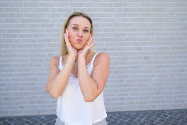Simpering blond woman holding her hands to her cheeks pursing her lips for the camera
