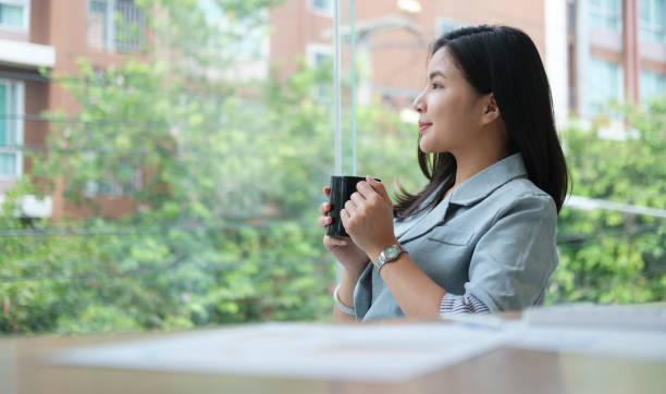 istock Peaceful businesswoman drinking coffee and looking through window in office, thinking about future or seeking for inspiration. 1415725348