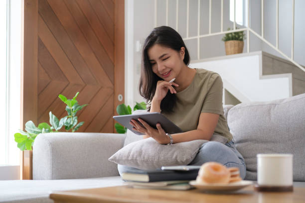 istock Smiling young woman in casual clothes relaxing on comfortable sofa at home and using digital tablet. 1415725606