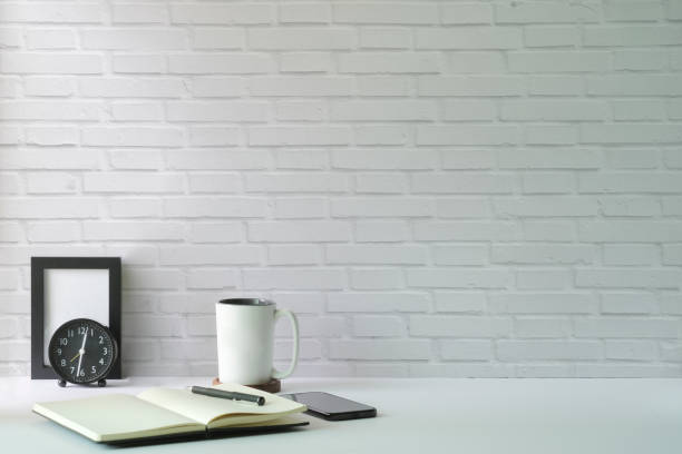 istock Minimal workplace with picture frame, coffee cup, mobile phone and notebook on white table. Copy space for advertise text or information content. 1415725812