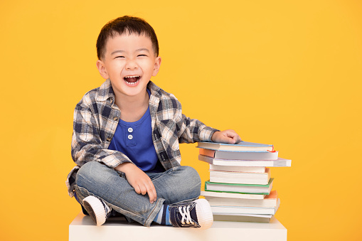 Happy kid sitting with books isolated on yellow background