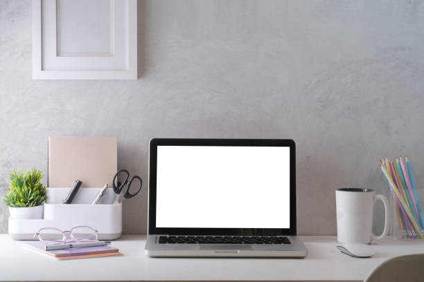 istock Mockup laptop with empty display, coffee cup, books and picture frame on white table. 1415726567