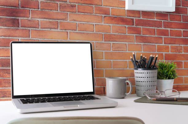 istock Mock up computer laptop, coffee cup, books and houseplant on white table against brick wall. 1415726575
