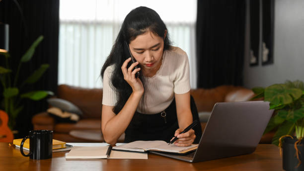 istock Busy young businesswoman having phone conversation and making notes on notebook during working from home. 1415727279