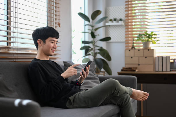 istock Relaxed young man in sweater using mobile phone, spending leisure time at home in winter or autumn weekend. 1415727429