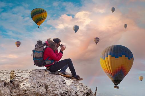 Young man shooting photos of hot air balloons flying in red and rose valley in Goreme in Cappadocia in Turkey