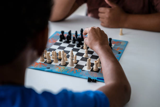 istock Hands in action. Two black kids play chess at home. 1415730496