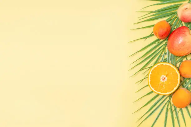 Palm leaves and tropical fruits on yellow background - creative summer background for design
