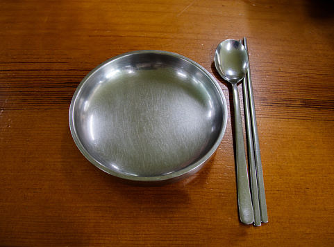 Metal plates, spoons and chopsticks on a wooden table