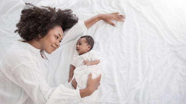 closeup portrait of beautiful young african american mother day girl kiss healthy newborn baby sleep in bed flat lay copy space. healthcare medical love black woman lifestyle mother's day, top view - baby stockfoto's en -beelden