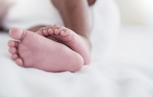 Closeup feet of newborn African black baby isolated on white hospital bed sheet. Healthcare and medical love lifestyle father or motherâs day background concept banner