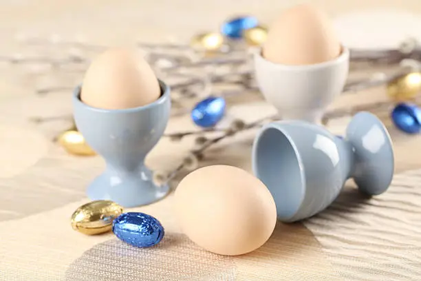 Eggs in white and blue eggcups with catkins and little chocolate eggs in foil. 