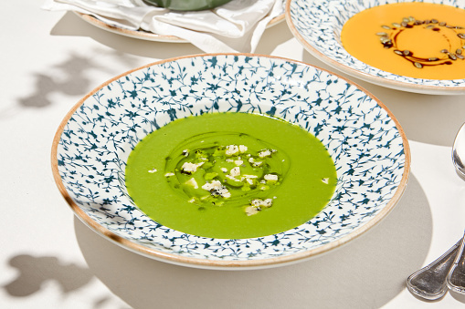 Composition with vegetable soup in ceramic bowl. Green soup with broccoli and cheese on summer day. Italian soup with green pea. Vegan menu. Hot dishes. Vegetables food. Eat less meat