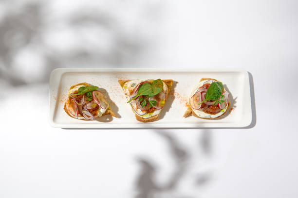 istock Aesthetic composition with tomato bruschetta on white background with harsh shadows. Italian bruschetta with tomatoes and cheese on fine dining in summer. Elegant menu concept. 1415737862